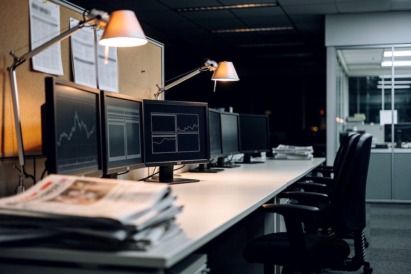 An empty editorial newsroom at night, desks and lamps lit
